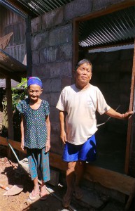 Herr und Frau Phia Xiong stehen vor einer gemauerten Toilette. Der Türrahmen aus Holz und das Wellblechdach sind fertig.