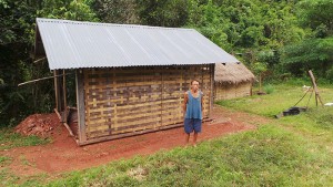 Herr Ya Ning Vangsteht vor seiner neuen Hütte. Sie besteht aus einer Holzkonstruktion, die mit Pastmatten verkleidet ist. Ein Wellblech schützt sie vor Regen. 