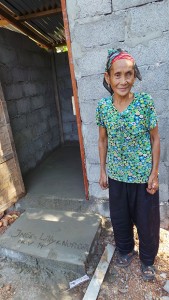 Frau Me Tau Sai Phia steht vor ihrer gerade fertig gewordenen Toilette. Der Beton am Fußboden und die Stufe vorm Eingang sind noch ganz frisch.