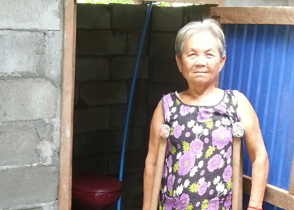 Frau Gong steht gestützt auf Gehhilfen vor ihrer neuen Toilette