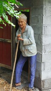 Frau Tau Tum steht auf einen Stock gestützt vor ihrer Toilette